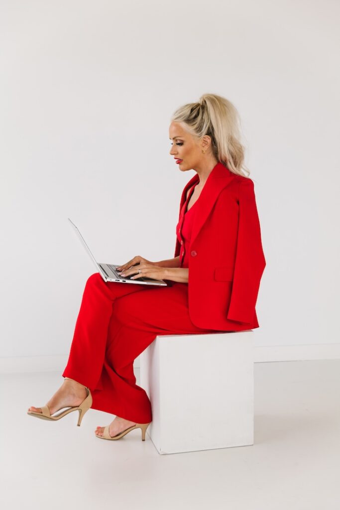 Personal brand photo of a woman in a red power suit, working on her laptop.