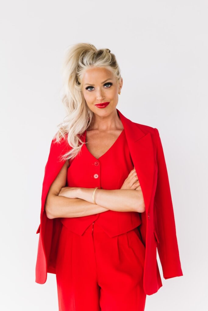 Bold brand photo of a female entrepreneur in a red suit, posed against a white studio wall.